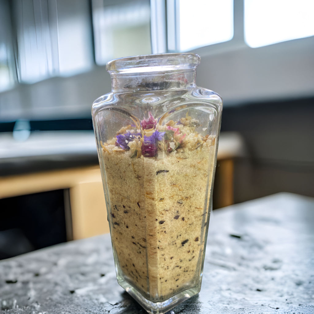 Large Clear Wedge Jar with Essence of Jojoba and Olive Oil Pure Ancient Himalayan Sea Salt with Flowers of Lavender Calendula Rose Petals has Essential Oils Tea Tree Lavender and Chamomile Topped with Don't Forget Me Flowers and Purple Gomphrena.