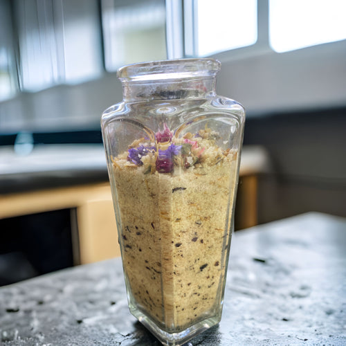 Large Clear Wedge Jar with Essence of Jojoba and Olive Oil Pure Ancient Himalayan Sea Salt with Flowers of Lavender Calendula Rose Petals has Essential Oils Tea Tree Lavender and Chamomile Topped with Don't Forget Me Flowers and Purple Gomphrena.