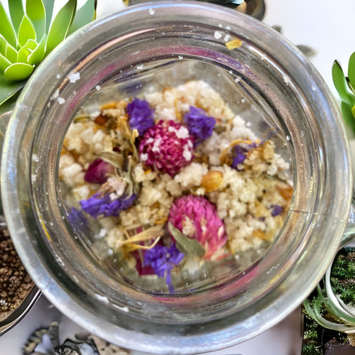 Large Clear Wedge Jar with Essence of Jojoba and Olive Oil Pure Ancient Himalayan Sea Salt with Flowers of Lavender Calendula Rose Petals has Essential Oils Tea Tree Lavender and Chamomile Topped with Don't Forget Me Flowers and Purple Gomphrena.